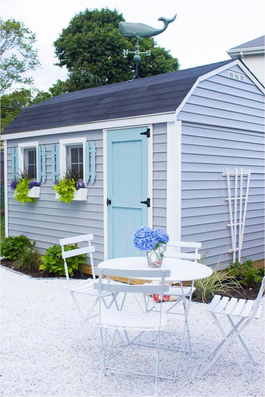 A blue outdoor shed with a whale weather vane & white table