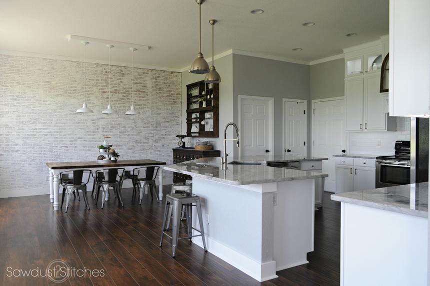 Kitchen with white cabinetry, white-washed brick wal
