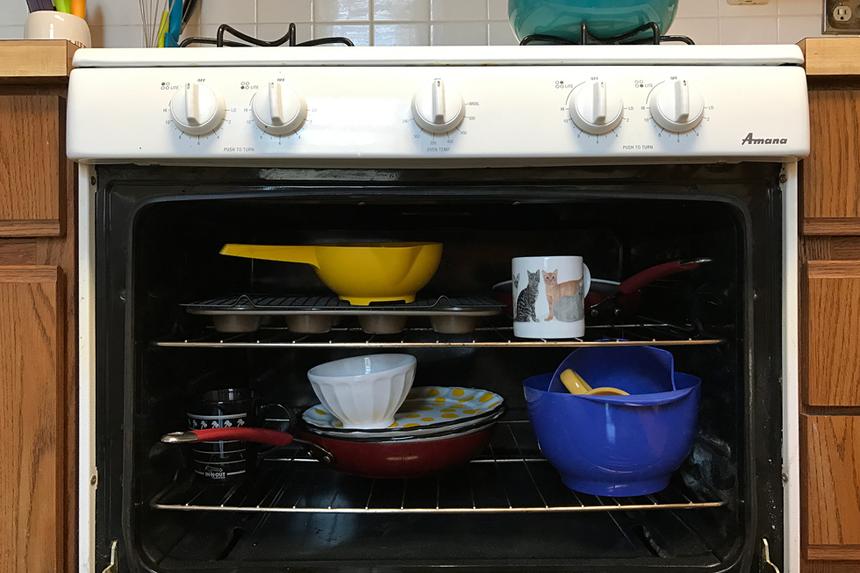 Dishes, pans, and mugs in a white oven that is open