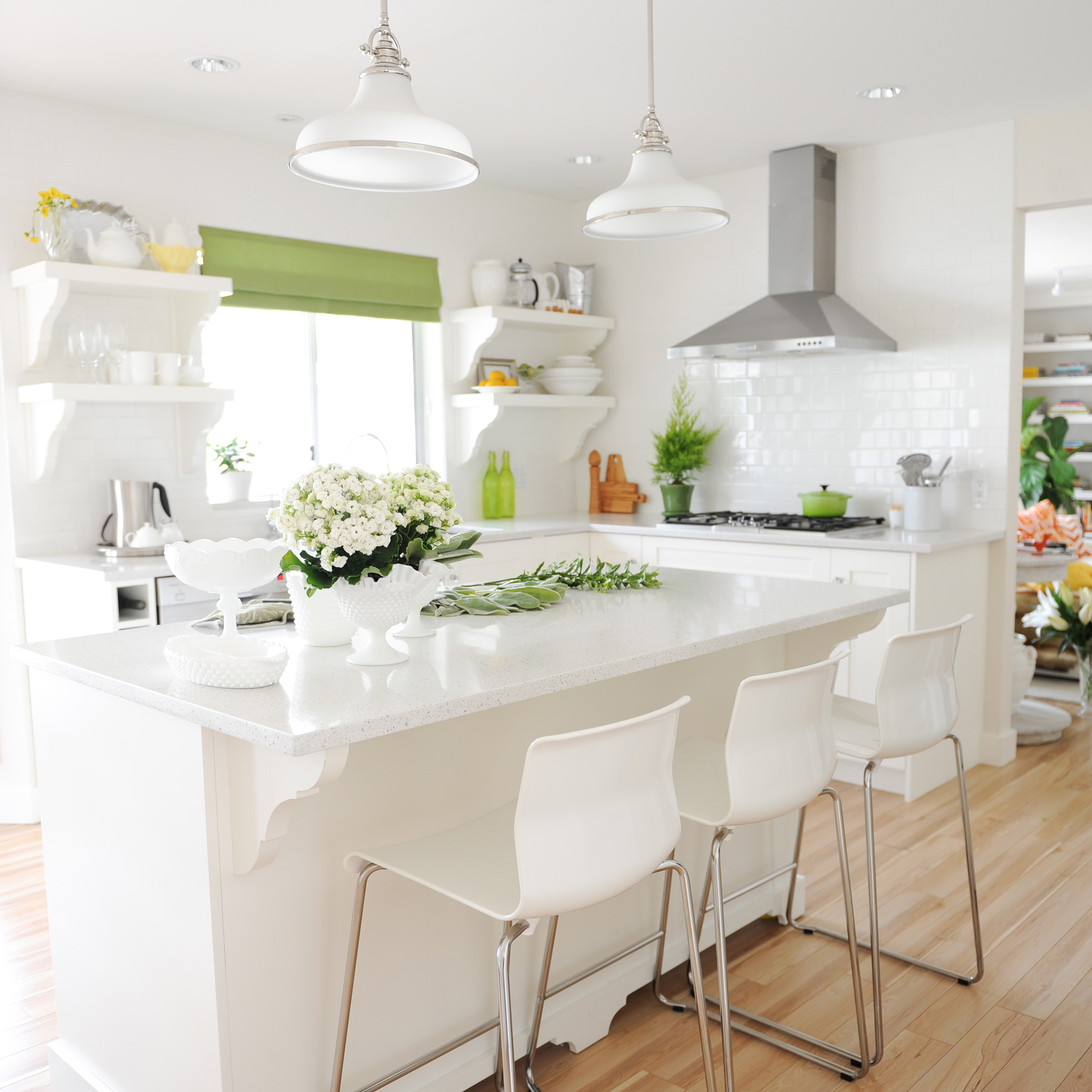 A white, bright kitchen with green curtains and accents